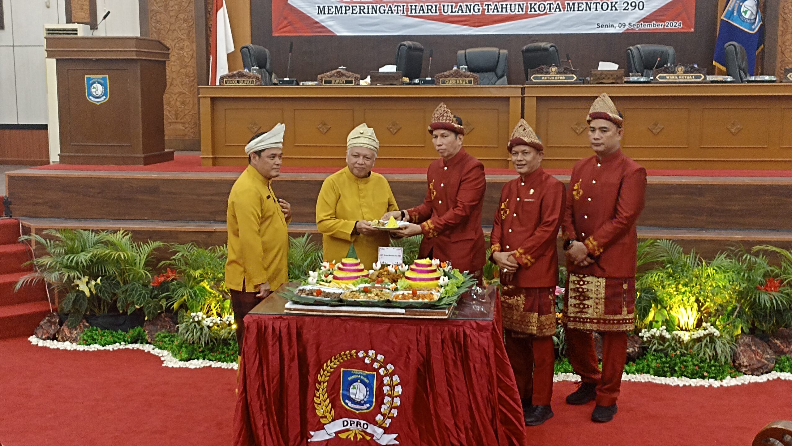 Caption: Ketua DPRD Kabupaten Bangka Barat, Marudur Saragih memotong tumpeng HUT ke-290 Kota Mentok diberikan kepada Bupati Babar Sukirman, di Gedung Mahligai Betason II, pada Senin (9/9/2024).